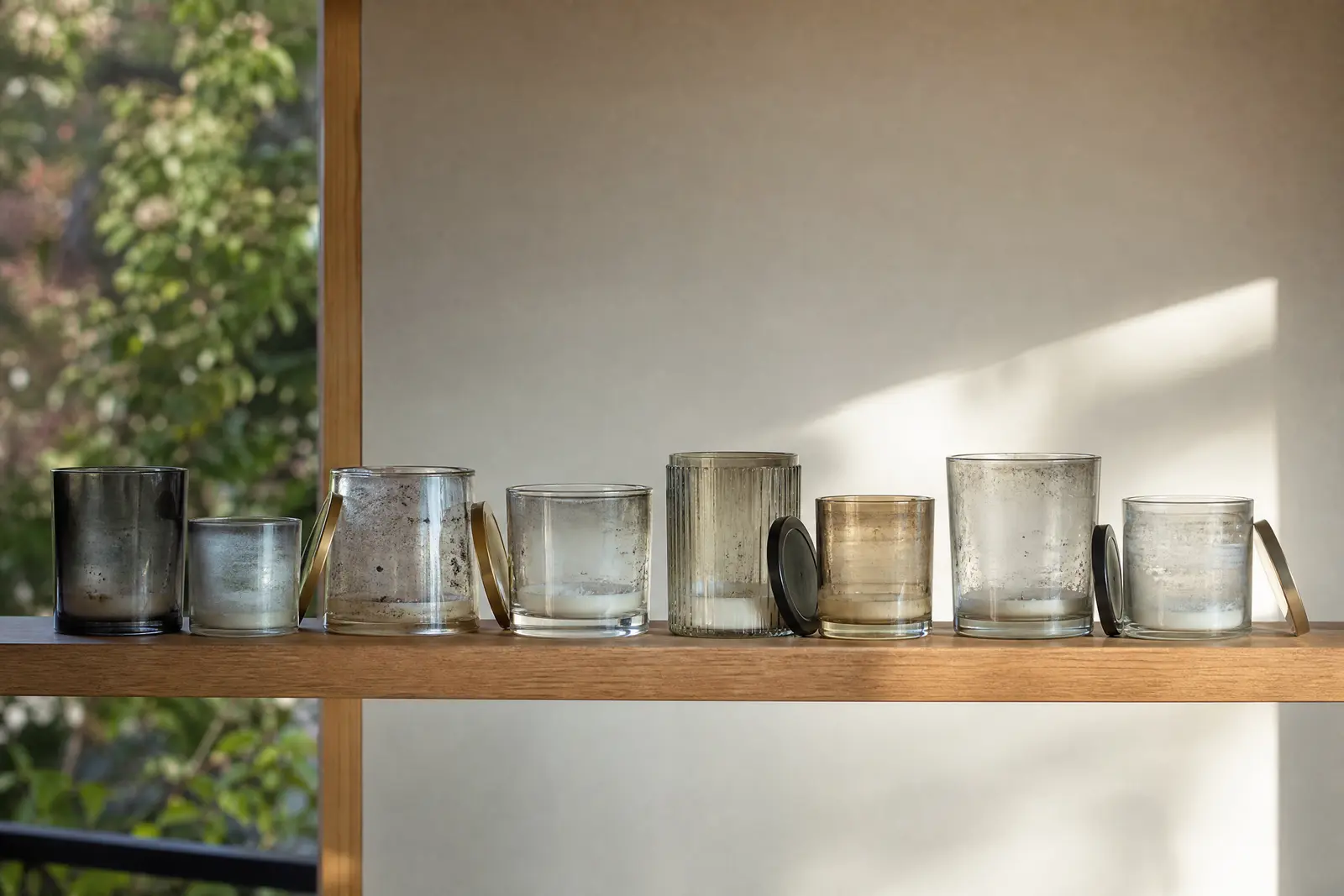 Eight used candle jars of different sizes lined up on a wooden shelf